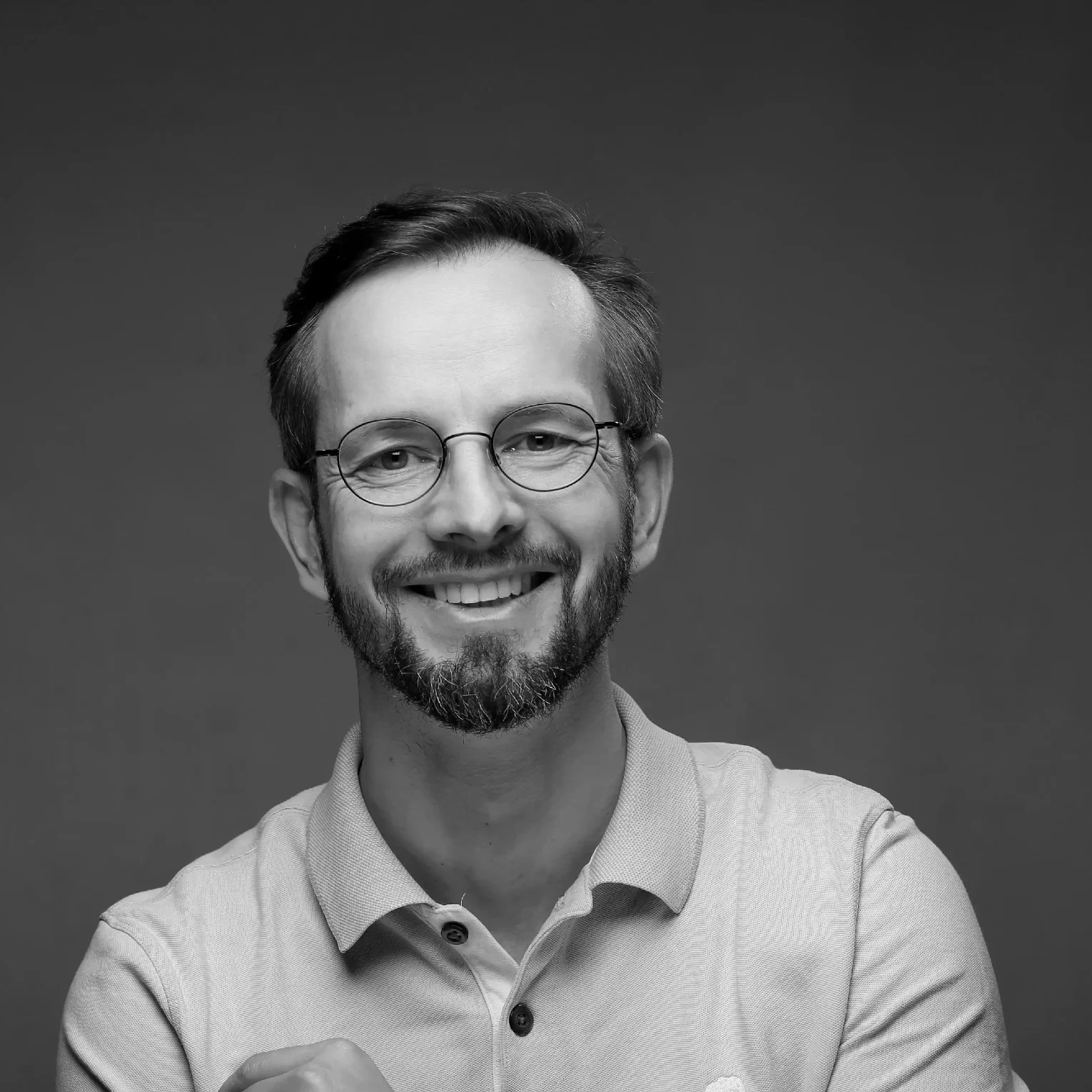 Ein lächelnder Mann mit Brille trägt ein helles Polohemd.